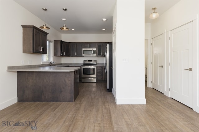 kitchen featuring kitchen peninsula, stainless steel appliances, hardwood / wood-style floors, dark brown cabinetry, and sink