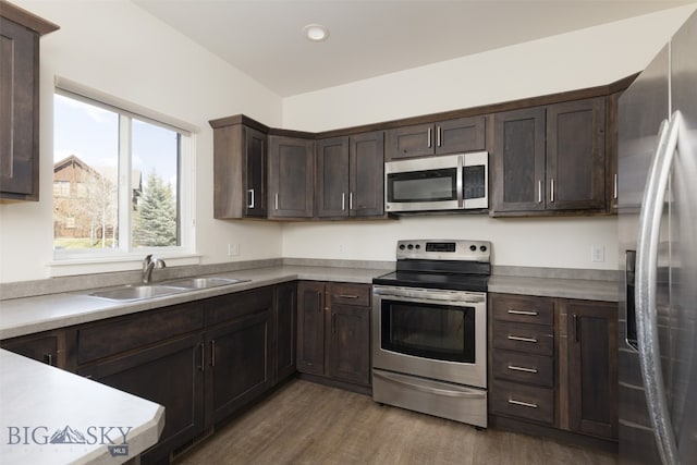 kitchen with appliances with stainless steel finishes, hardwood / wood-style flooring, sink, and dark brown cabinetry