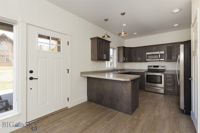 kitchen featuring appliances with stainless steel finishes, kitchen peninsula, hardwood / wood-style flooring, and dark brown cabinets