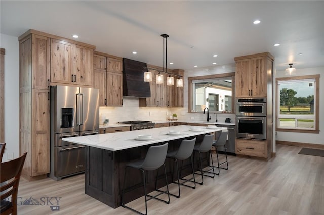 kitchen with appliances with stainless steel finishes, hanging light fixtures, a center island, light stone countertops, and custom range hood