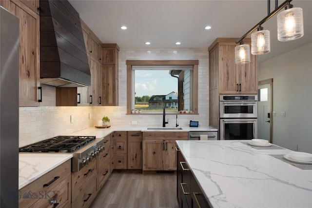 kitchen featuring sink, decorative light fixtures, appliances with stainless steel finishes, custom range hood, and light stone countertops