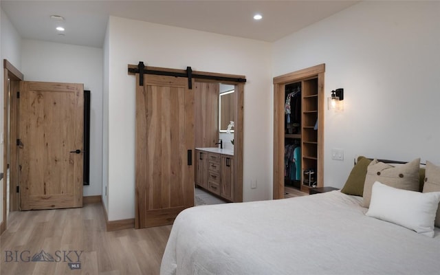 bedroom with light hardwood / wood-style flooring, connected bathroom, a barn door, a spacious closet, and a closet