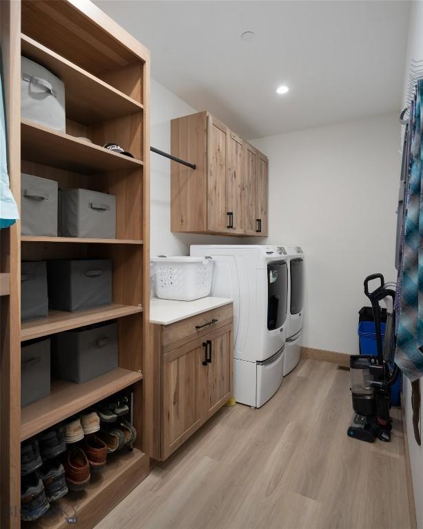 clothes washing area with cabinets, washer and dryer, and light hardwood / wood-style floors