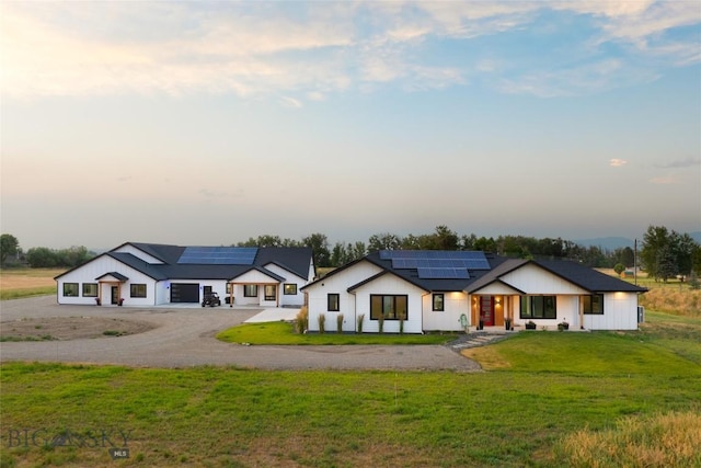 back house at dusk featuring a garage, a lawn, and solar panels