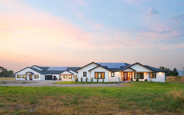 back house at dusk with a lawn and solar panels