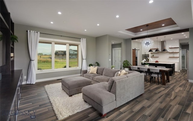 living room with a notable chandelier, a tray ceiling, and dark hardwood / wood-style floors