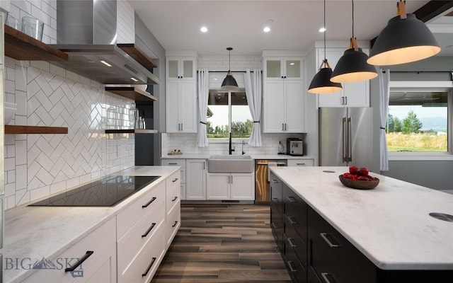 kitchen featuring wall chimney exhaust hood, sink, decorative light fixtures, stainless steel appliances, and white cabinets