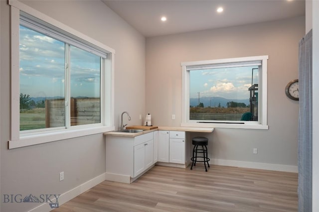 bar featuring white cabinetry, light wood-type flooring, sink, and a wealth of natural light