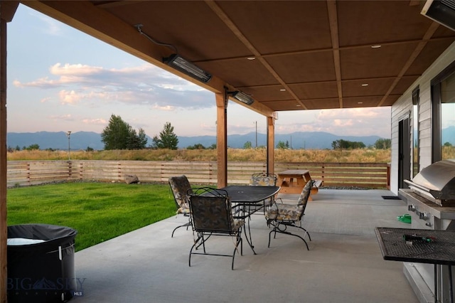 patio terrace at dusk with a mountain view, area for grilling, and a lawn