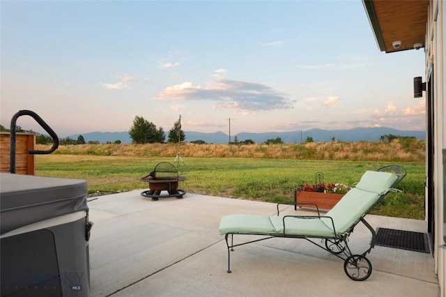 patio terrace at dusk featuring a rural view, a mountain view, a fire pit, and a lawn