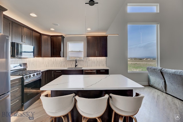 kitchen with stainless steel appliances, hanging light fixtures, decorative backsplash, sink, and light hardwood / wood-style floors