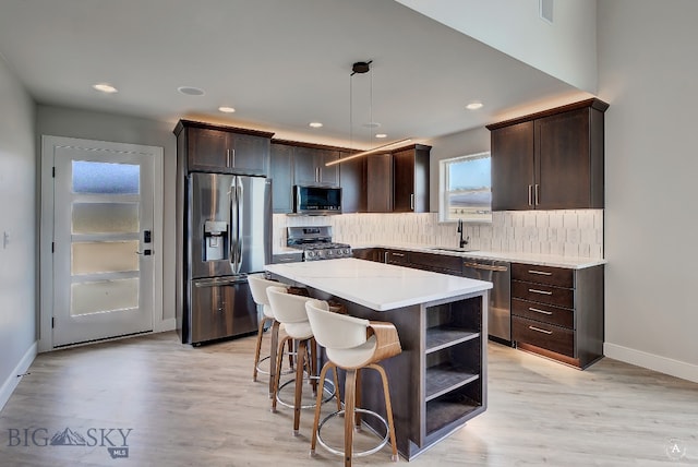 kitchen featuring appliances with stainless steel finishes, light hardwood / wood-style floors, decorative light fixtures, decorative backsplash, and a center island