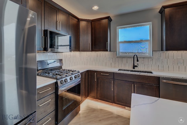 kitchen with stainless steel appliances, sink, dark brown cabinetry, light wood-type flooring, and light stone countertops