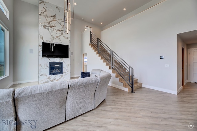 living room with a high end fireplace, light wood-type flooring, and a towering ceiling