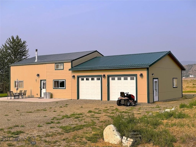 exterior space featuring a standing seam roof, metal roof, dirt driveway, and a patio