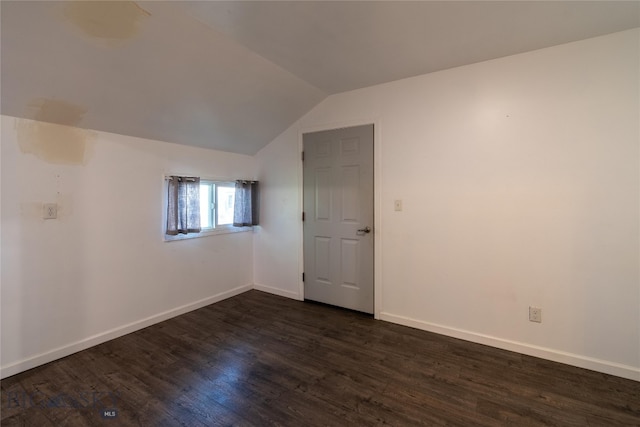 spare room featuring dark wood-type flooring and vaulted ceiling