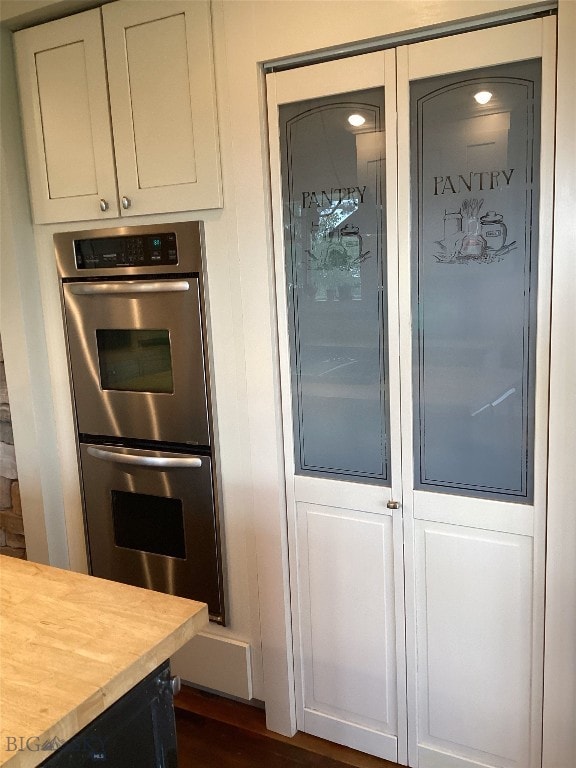 kitchen featuring butcher block counters, double oven, white cabinets, and dark wood finished floors