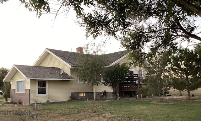 rear view of property featuring a chimney, a lawn, and roof with shingles