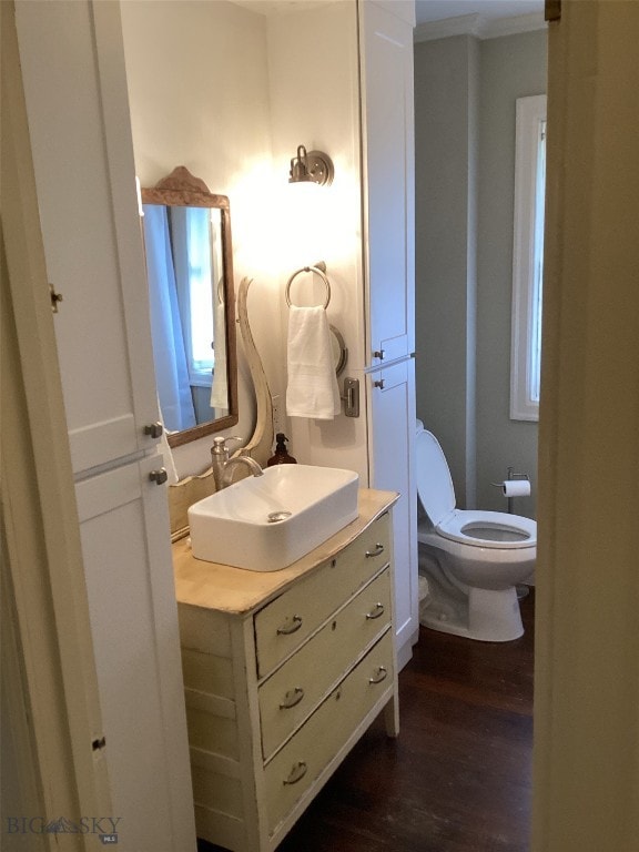 half bathroom with toilet, ornamental molding, wood finished floors, and vanity