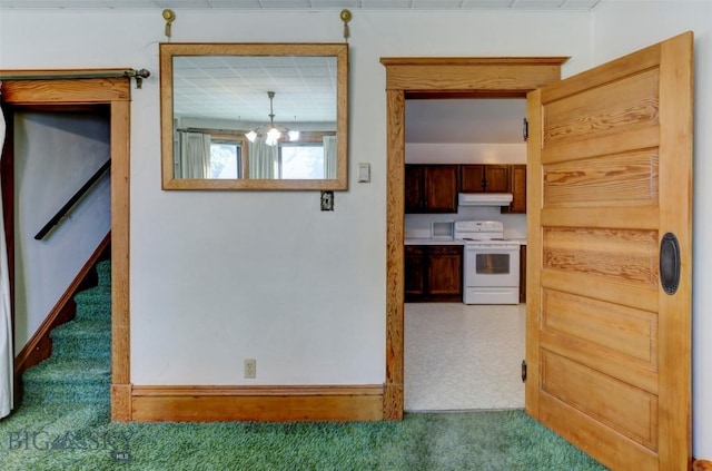 kitchen featuring a notable chandelier, under cabinet range hood, carpet floors, baseboards, and white range with electric stovetop