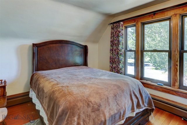 bedroom featuring hardwood / wood-style flooring, vaulted ceiling, multiple windows, and baseboard heating