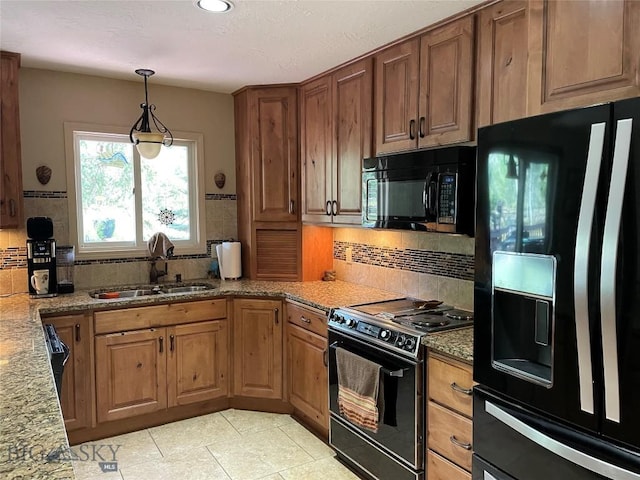 kitchen featuring brown cabinetry, a sink, backsplash, black appliances, and hanging light fixtures