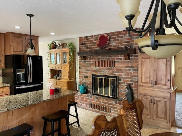 kitchen featuring hanging light fixtures, a breakfast bar, a brick fireplace, stone countertops, and black fridge with ice dispenser