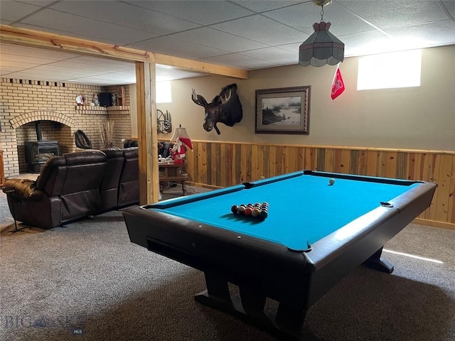 recreation room with wooden walls, a wood stove, carpet floors, a wainscoted wall, and a drop ceiling