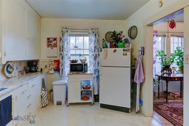 kitchen featuring plenty of natural light, white fridge, and white cabinets