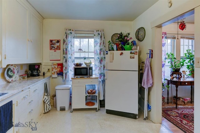 325 N 3rd St, Livingston, MT 59047 - kitchen with freestanding refrigerator, stainless steel microwave, white cabinetry, light flooring, and light stone counters