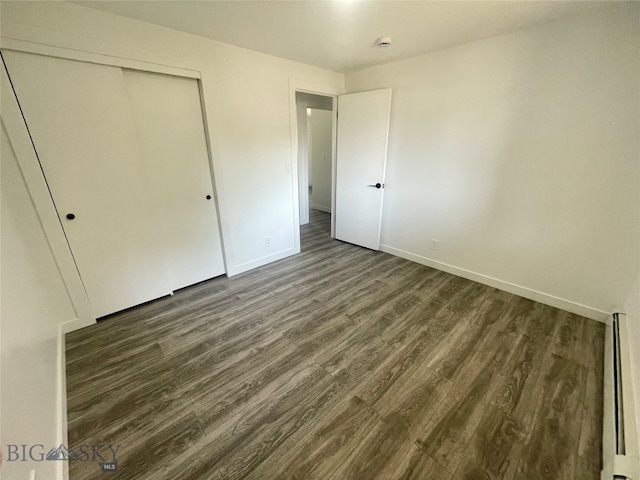 unfurnished bedroom with a closet, wood-type flooring, and a baseboard heating unit