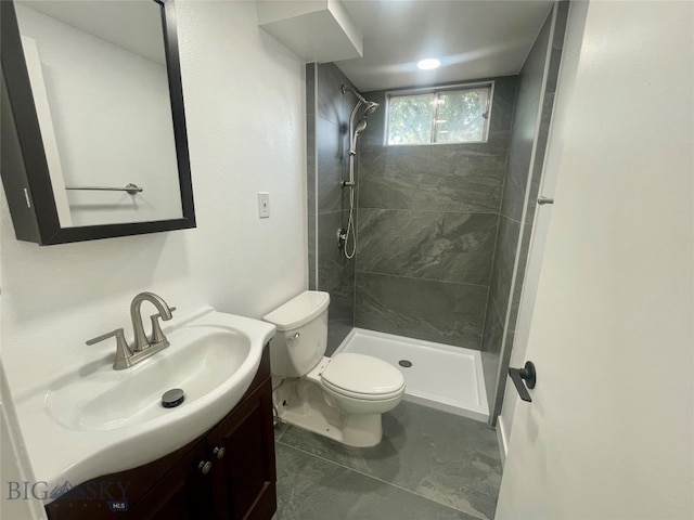 bathroom with vanity, toilet, a tile shower, and tile patterned floors