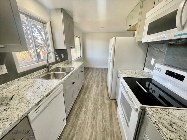 kitchen with sink, light stone countertops, white appliances, and light hardwood / wood-style floors