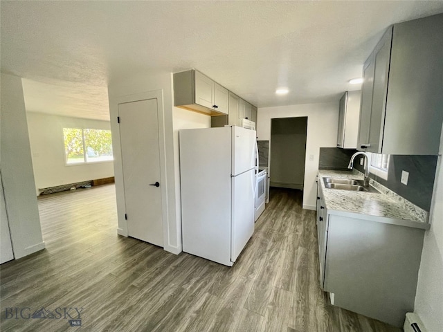 kitchen with light wood-type flooring, white appliances, baseboard heating, sink, and tasteful backsplash