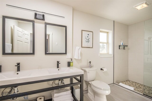 bathroom with dual vanity, toilet, and a tile shower