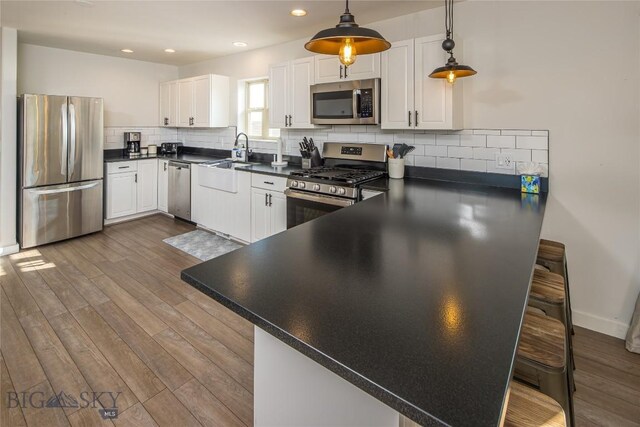 kitchen with a kitchen bar, tasteful backsplash, stainless steel appliances, decorative light fixtures, and hardwood / wood-style flooring