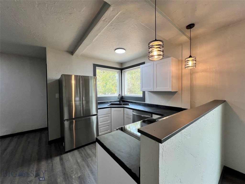 kitchen featuring dark countertops, appliances with stainless steel finishes, white cabinets, a sink, and a peninsula