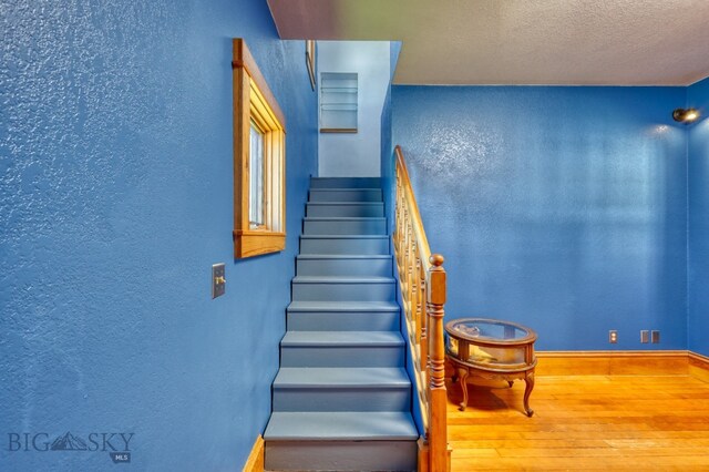 stairs featuring a textured ceiling and hardwood / wood-style flooring