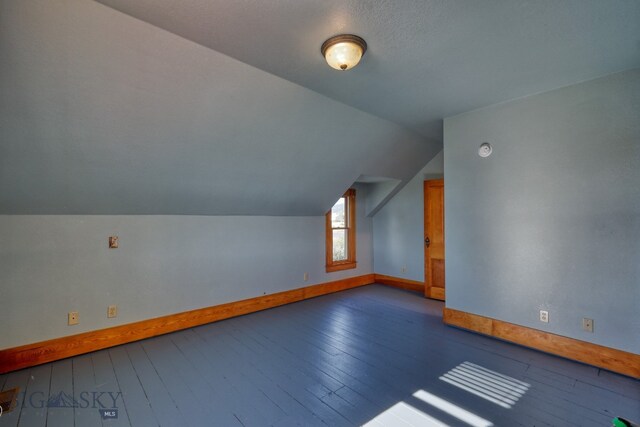 additional living space featuring a textured ceiling, hardwood / wood-style flooring, and vaulted ceiling