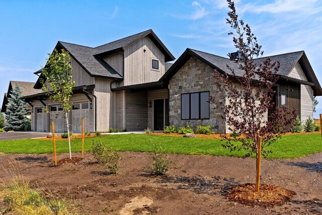 view of front facade featuring roof with shingles, driveway, stone siding, and a front lawn