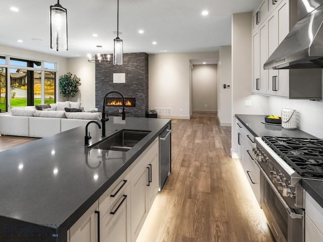 kitchen with wall chimney range hood, stainless steel appliances, sink, pendant lighting, and white cabinetry