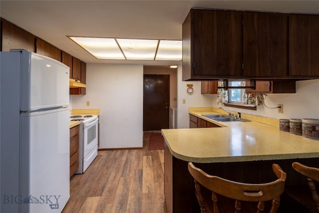 kitchen with a kitchen bar, kitchen peninsula, light hardwood / wood-style floors, white appliances, and sink