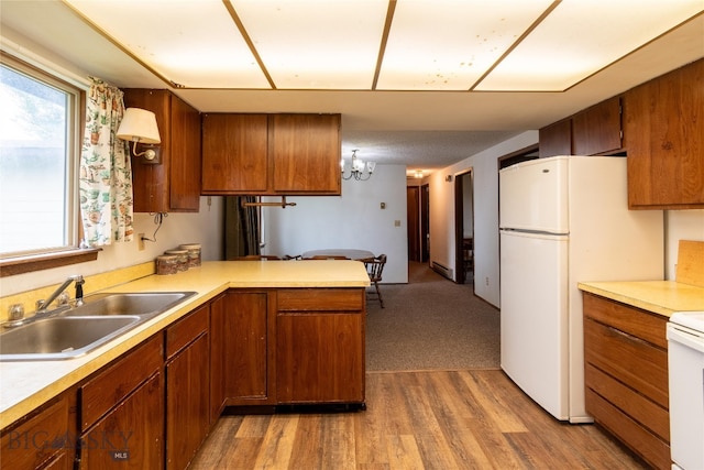 kitchen with carpet, white refrigerator, sink, a chandelier, and kitchen peninsula