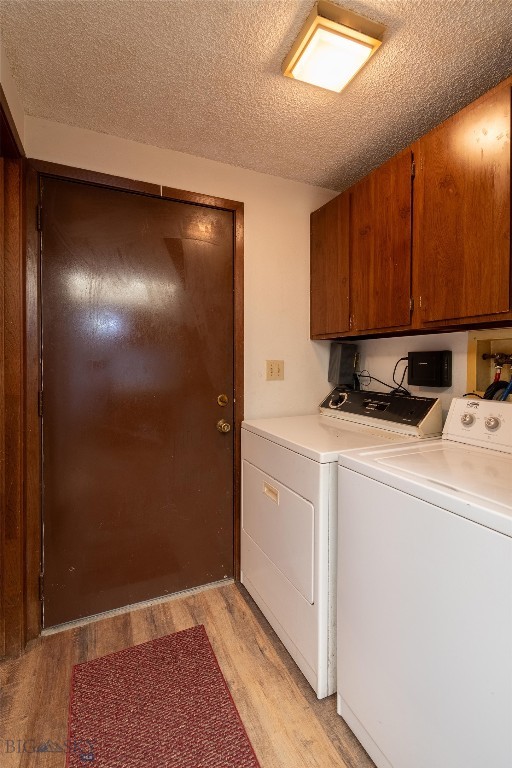 clothes washing area with light hardwood / wood-style flooring, cabinets, a textured ceiling, and separate washer and dryer