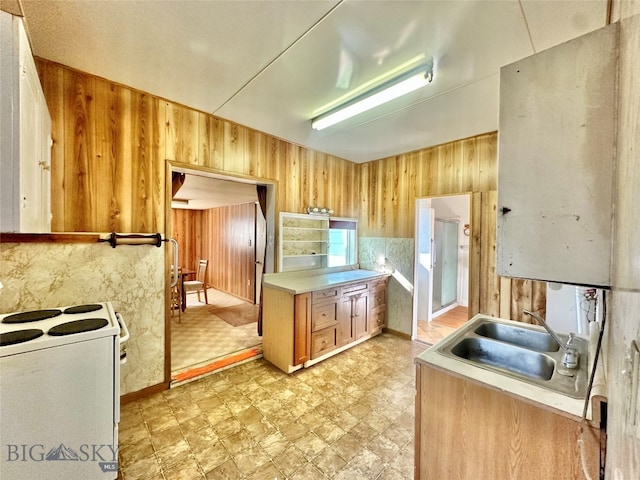 kitchen featuring electric stove, wooden walls, sink, and light brown cabinets