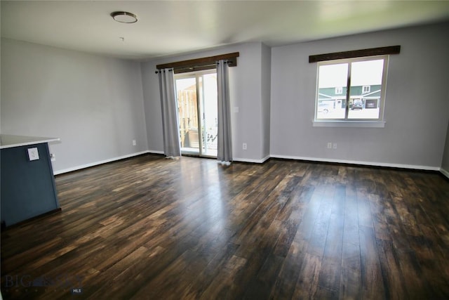 spare room featuring dark wood-style floors, plenty of natural light, and baseboards