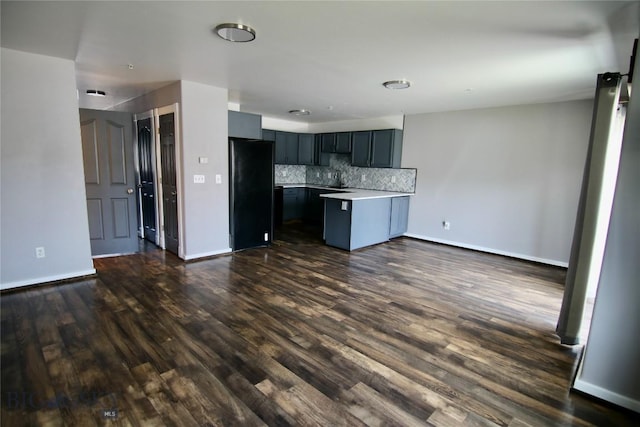 kitchen featuring open floor plan, dark wood-type flooring, freestanding refrigerator, light countertops, and backsplash