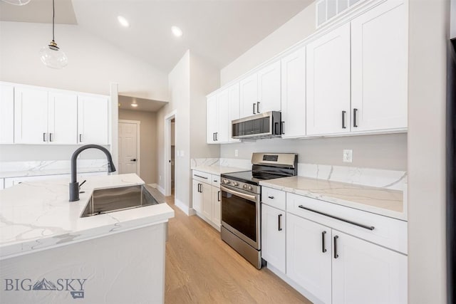 kitchen with pendant lighting, lofted ceiling, white cabinetry, appliances with stainless steel finishes, and sink