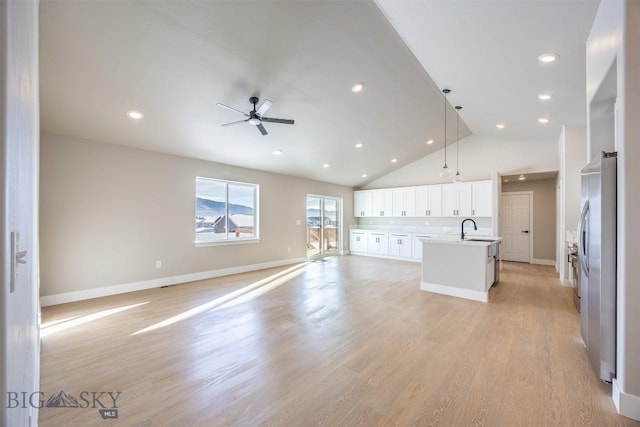 unfurnished living room with high vaulted ceiling, light wood-type flooring, ceiling fan, and sink