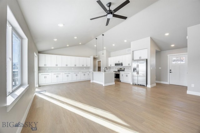 kitchen with appliances with stainless steel finishes, an island with sink, pendant lighting, a wealth of natural light, and white cabinetry